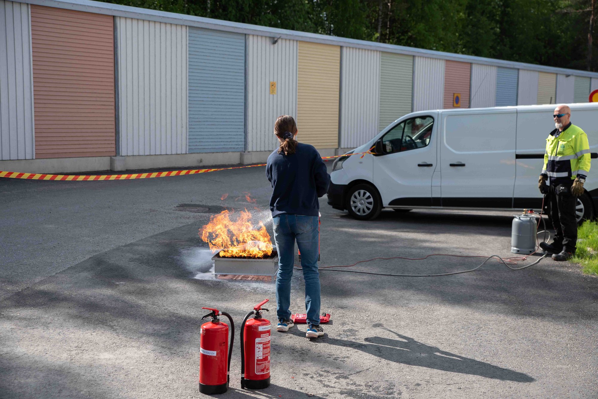 Henkilö alkusammutusharjoituksessa sammuttamassa sammuttimella tulta. Kuvassa kouluttaja seuraa tilannetta.