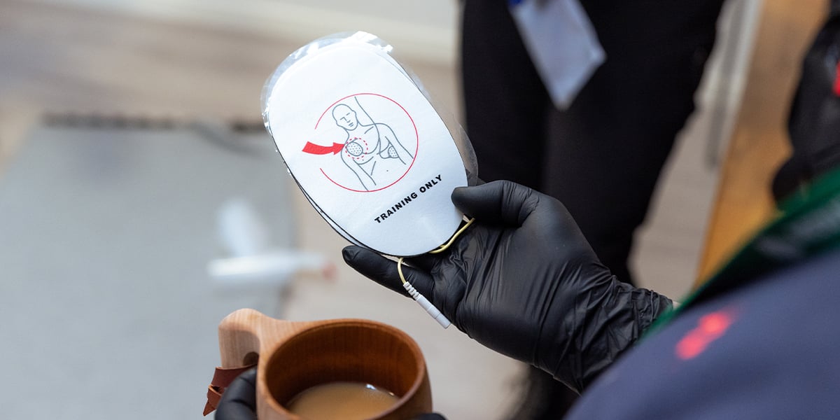 Ihmisellä kädessä elvytyksessä käytettävä väline ja kahvikuppi.